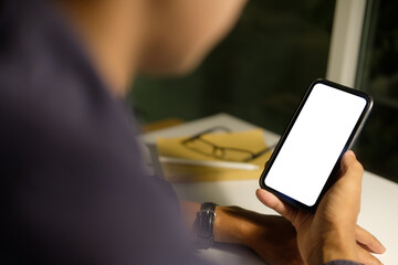 Wall Mural - close up of hands holding a smartphone with blank white screen, against a dimly lit background.
