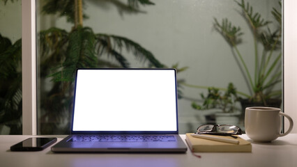 Fototapete - Laptop with a blank screen, cup of coffee and mobile phone against a backdrop of greenery outside the window.