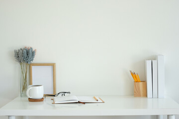 Wall Mural - White desk featuring an open notebook, a white coffee mug, glasses, and a pencil.