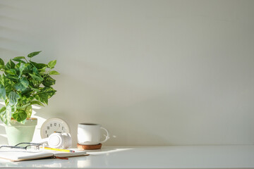 Wall Mural - Comfortable workspace arrangement of a potted plant, notebook, a coffee mug and a clock.