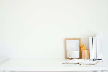 Wall Mural - A wooden photo frame, a cup of coffee, wooden holder, book and glasses on white desk.