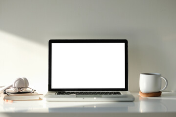 Fototapete - Laptop with white screen notebook, glasses, headphones and a coffee mug on white table.