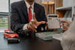 © kamiphotos - a car salesman is explaining the details of a car and the pricer that a buyer is interested in, the showroom sales manager explained the amount of interest