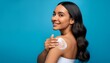 © adobedesigner - Gorgeous girl with soft makeup applying moisturizing skincare cream on shoulder isolated over blue background.