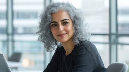 Wall Mural - Smiling Middle-Eastern woman with curly gray hair working in a modern office.