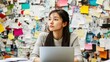 © yusufadi - Thoughtful young woman working on her laptop in front of a colorful inspiration board.  A scene of contemplation and creative brainstorming.