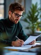 © SOANDLI - Businessman reviewing documents at work – Serious young man in a dark green sweater and glasses, analyzing papers at his desk in a bright office.