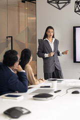 Wall Mural - Serious project manager woman presenting business plan to colleagues, diverse team of investor, speaking at electronic board in meeting room, holding presentation, seminar, training. Vertical shot