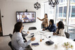 © fizkes - Diverse group of company employees talking to remote colleagues on video conference call chat, looking at large TV screen, meeting for online and offline global training, Internet communication