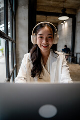 Poster - Young asian businesswoman wearing headphones working remotely on laptop in a cafe, enjoying online meeting