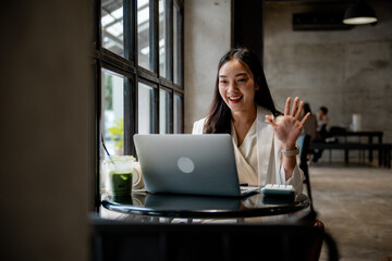 Poster - Asian businesswoman waving hand while having video conference on laptop in cafe