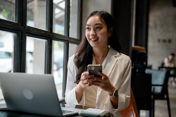 Poster - Young asian businesswoman using smartphone and laptop while working remotely in a cafe