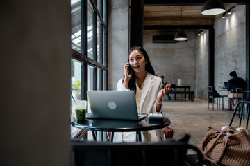 Poster - Asian businesswoman managing her business, talking on the phone and working on her laptop in a modern cafe