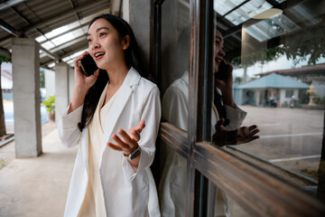Poster - Young professional woman having a phone conversation while leaning against a window