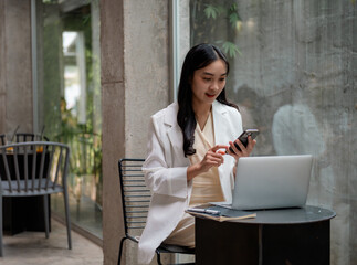 Poster - Young asian businesswoman using smartphone and laptop while working remotely in a modern cafe