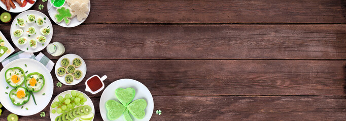 Poster - St Patricks Day breakfast or brunch corner border against a dark wood banner background. Variety of green and shamrock themed pancakes, toasts, eggs, fruits and meats. Above view. Copy space.