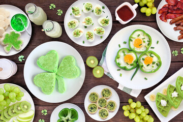 Poster - St Patricks Day breakfast or brunch table scene against a dark wood background. Assortment of green and shamrock themed pancakes, toasts, eggs, fruits and meats. Overhead view.