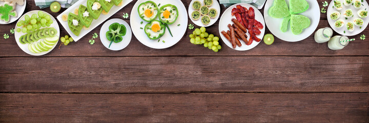 Aufkleber - St Patricks Day breakfast or brunch top border against a dark wood banner background. Variety of green and shamrock themed pancakes, toasts, eggs, fruits and meats. Above view. Copy space.