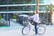 © Evgeniia Primavera - cute white girl 7 years old riding a bicycle in a modern neighborhood in an urban setting with modern glass buildings and palm trees in the background, looking confident