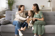 © fizkes - Three generations of women, grandmother, mother, little girl sitting together on sofa with beagle dog, enjoying warm, relaxed moments, exude sense of family bonding, care, and joy, in homey atmosphere