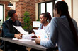 © DC Studio - Black professionals sitting at a meeting table, evaluating business proposals and strategies for startup company. African american colleagues having a group discussion in brick wall office.