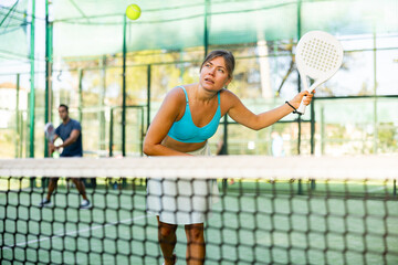 Wall Mural - Caucasian woman in tank top and skirt playing padel tennis match during training on court.