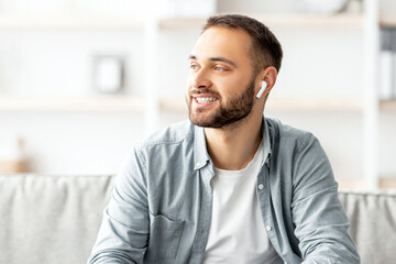 Poster - Smiling young man in earphones using laptop for online communication at home office. Millennial Caucasian freelancer having video call, chatting remotely via computer, indoors