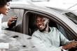 © Prostock-studio - Test drive. Cheerful black man sitting in driver seat of new car, choosing vehicle with his wife and daughter at auto dealership. African American family checking automobile before purchase