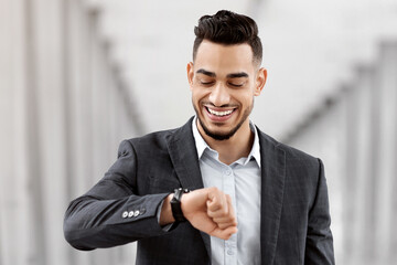 Wall Mural - Going To Flight. Arab Businessman Walking With Suitcase In Airport And Looking At Wristwatch, Handsome Middle Eastern Male Traveller Checking Departure Time On Watch, Ready For Air Trip, Copy Space