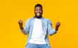 © Prostock-studio - Portrait of overjoyed black man celebrating success with clenched fists and euphoric face expression on yellow studio background with copy space