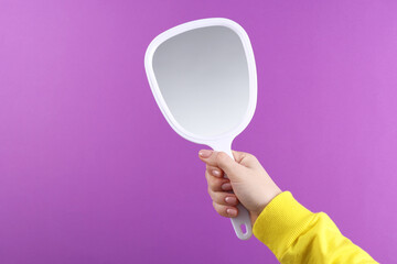 Woman holding handheld mirror on violet background, closeup. Space for text