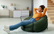 © Prostock-studio - Rest And Relax Concept. Calm black woman sitting on bean bag, listening to music, audio book, podcast, enjoying meditation for sleep and peaceful mind in wireless earphones, leaning back, copy space