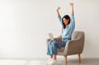 © Prostock-studio - Overjoyed millennial woman sitting in armchair with laptop, celebrating huge online win or success against white studio wall, copy space. Young lady enjoying big sale in web store
