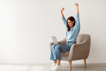 overjoyed millennial woman sitting in armchair with laptop, celebrating huge online win or success a