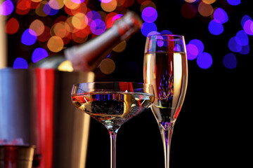 Champagne in glasses and ice bucket with bottle against black background with blurred lights, closeup