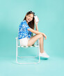 © sitthiphong - Happy smiling young Asian woman in summer sit in deckchair and holding smartphone mockup of blank screen in blue background.