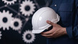 © AGCreative - professional engineer holding white safety helmet, symbolizing safety and engineering. background features abstract gears, representing industry and innovation