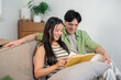 © bongkarn - A lovely Asian couple, a boyfriend and girlfriend, enjoy reading a book together on the sofa.