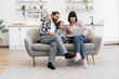 © sofiko14 - White family with mother, father, and young girl sitting on sofa watching laptop. Casual, joyful setting in modern living room. Happy, relaxed atmosphere with technology and bonding.