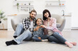 © sofiko14 - Happy Caucasian family with two adults and one child sitting in living room showing keys. They celebrate moving into new home, expressing joy and excitement.