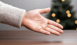 © hocine - Outstretched Hand Gesture for Offering or Invitation with a Soft Fuzzy Sweater in a Cozy Holiday Setting with Blurred Christmas Tree Lights in Background