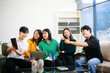 © laddawan - Group of young adults in casual wear, using laptops and headphones, enjoying teamwork,