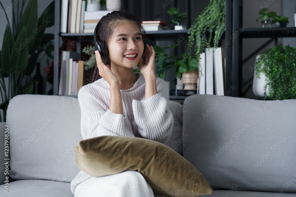 Asian woman sits on sofa listening to music in living room Stock Photo ...