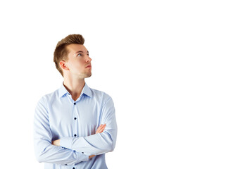 Fototapete - A young man in a striped blue shirt with arms crossed looks upward thoughtfully, isolated on a white background. Concept of thinking or confidence