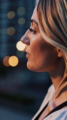 Poster - A creative side angle focusing on the wind gently lifting her blonde hair, with evening city bokeh adding a serene vibe to her quiet reflection.