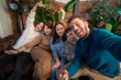 © Lomb - A happy group of diverse friends taking a selfie and laughing in a cozy indoor setting. A joyful, authentic moment of friendship, community, and creating memories together on a weekend.