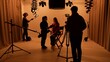 © kinomaster - Studio for photo video production with lighting equipment and cyclorama, team members preparing lights and camera, model sits on director chair talks with assistant.