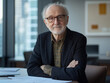 © Tobias - A senior man with glasses sits at a table with paperwork, arms crossed, gazing directly at the camera.