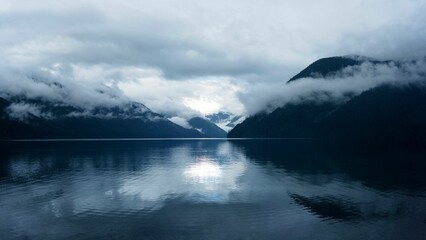 Poster - A serene lake with misty mountains reflecting in the water under a cloudy sky.