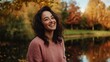 © Tatyana - Smiling woman by the water in autumn. Colorful leaves create a warm atmosphere around her joyful expression.